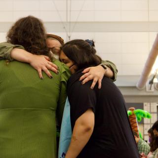 Three young people hugging. One of them is facing the camera and has their eyes closed.