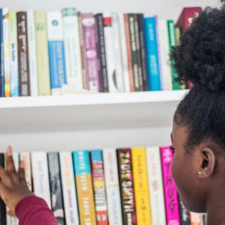 A young person reaches for a book on a book shelf.
