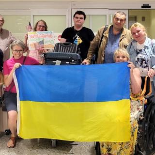 A group of people in an airport pose together while some of them hold up a large Ukrainian flag. 